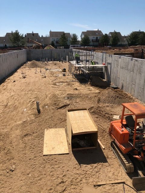 Construction site with excavated dirt, concrete walls, and an orange excavator in the foreground.
