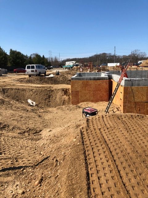 Construction site with dirt trenches, a white van, and a brick foundation under a clear blue sky