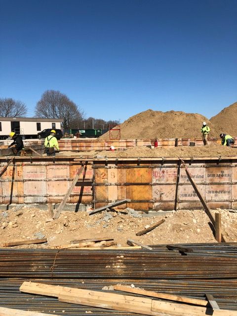 Construction workers on a foundation site, with wooden formwork and clear blue sky.