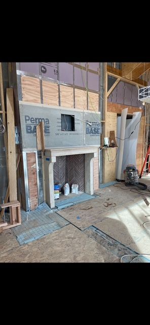 Small unfinished model house with doorway and windows in a construction workshop, surrounded by lumber.