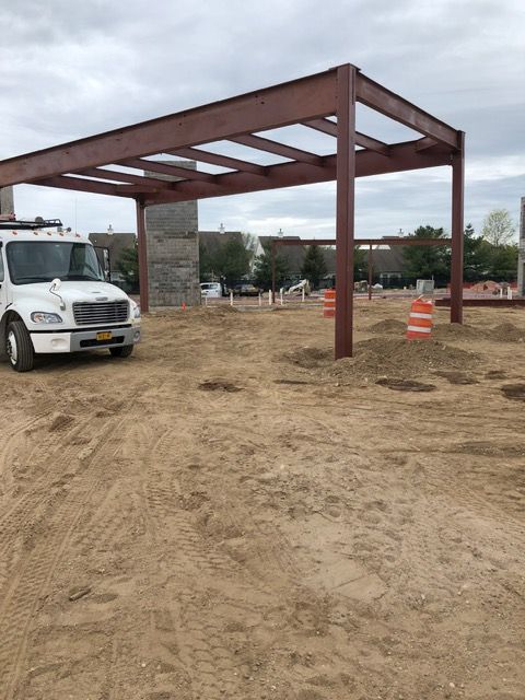 Partially built steel canopy on a dirt lot with a white van and orange traffic cones