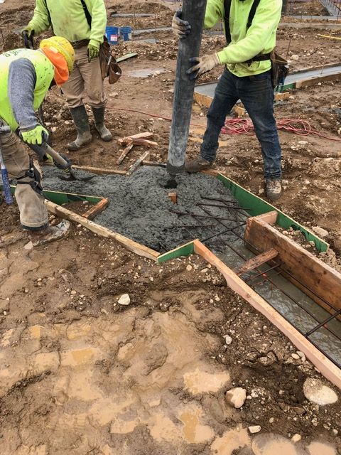 Construction workers pouring concrete into a wooden form on muddy ground outdoors