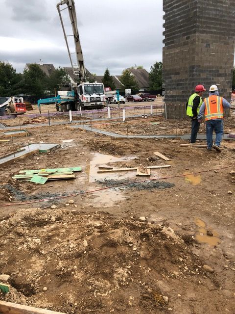 Construction site with crane, workers in safety vests, and a brick structure under cloudy skies