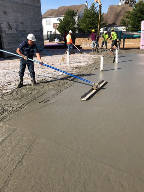 Workers leveling fresh concrete at a construction site with long-handled tools
