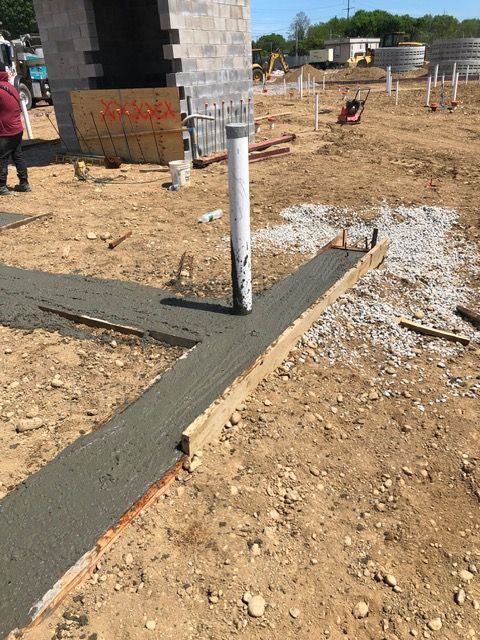 Fresh concrete walkway crossing a dirt construction site beside a brick structure and white pipe.