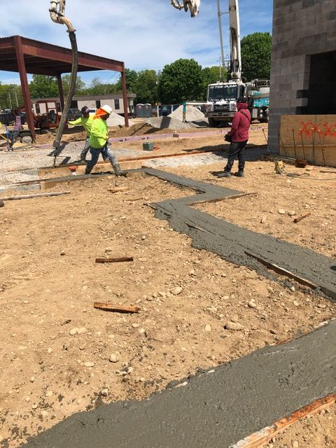 Construction workers pouring concrete on a site with rebar and unfinished structures.