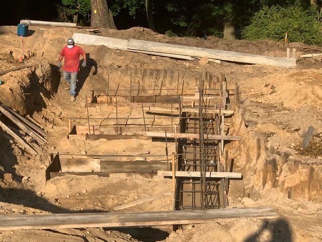 Worker in red shirt at a construction site beside a deep excavation with wooden and rebar supports