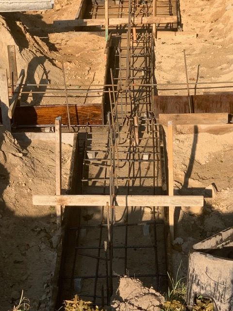 Concrete rebar framework in a trench, viewed from above at a construction site.
