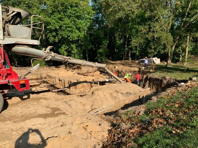 Excavator and workers at a muddy construction site with a collapsed trench beside a road