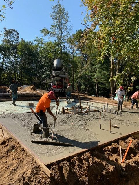 Workers pour concrete for a foundation at a wooded construction site.