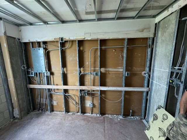 Exposed wall framing and wiring in an unfinished room with cardboard insulation backing and concrete floor