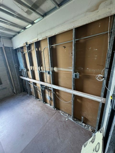 Partially demolished interior wall with exposed studs, wiring, and insulation in a renovation site