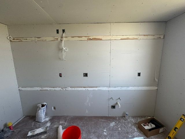Bare unfinished room with white drywall, exposed wiring, and construction tools on the floor.