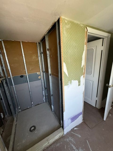 Bathroom under renovation with exposed studs, drywall, and an open door to a white toilet room