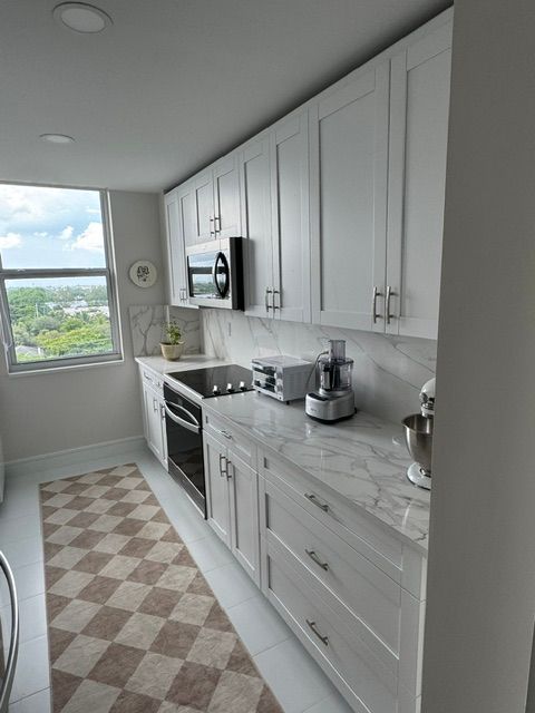 Bright narrow galley kitchen with white cabinets, stainless appliances, and checkered runner rug