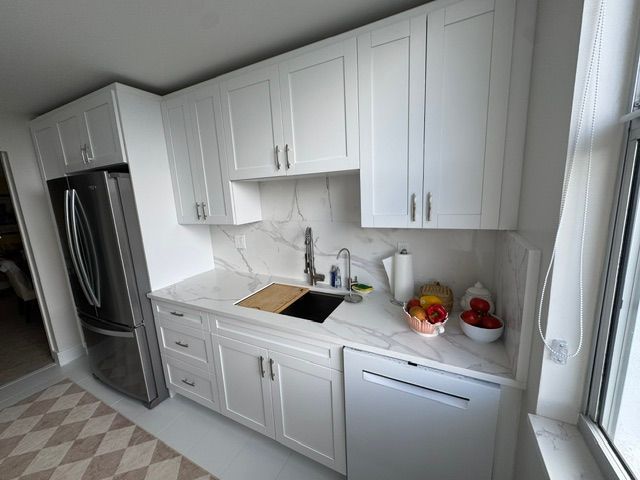 White kitchen with stainless fridge, sink, dishwasher, and fruit on the counter