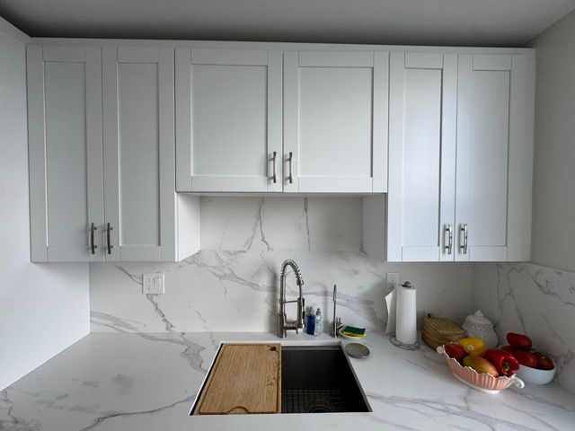 Modern white kitchen with marble backsplash, sink, cutting board, and fruit bowl on the counter