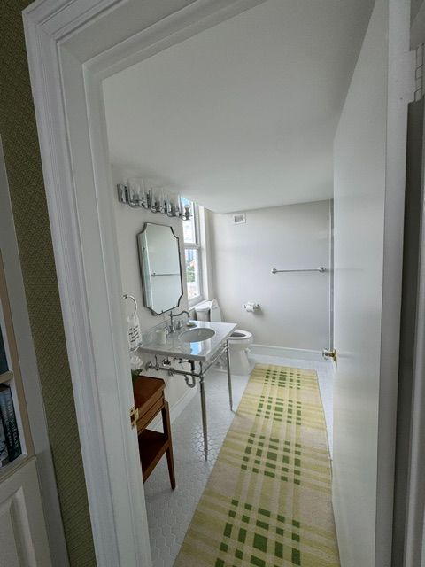 Bright white bathroom with sink, mirror, and a green patterned runner rug.