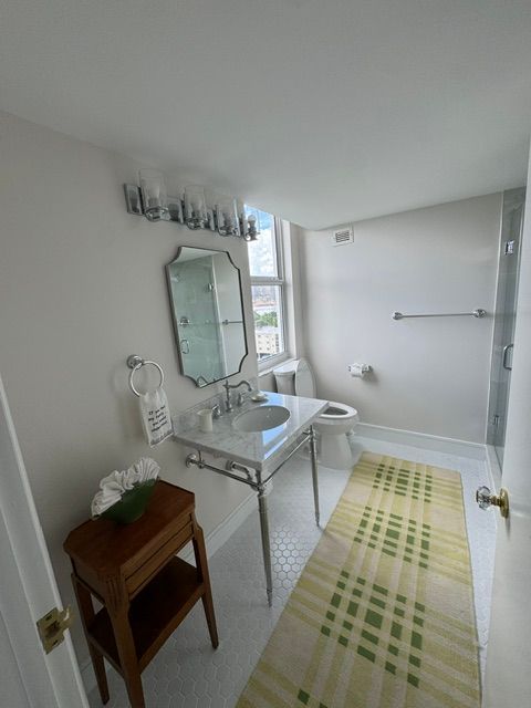 Bright bathroom with sink, mirror, tub, and green-striped rug