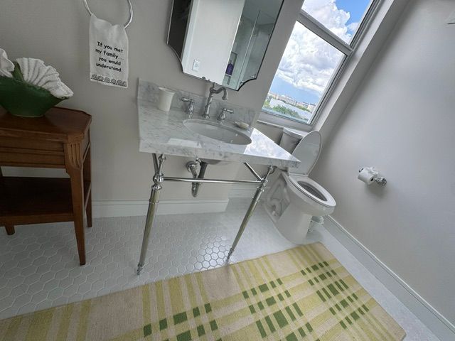 Bright bathroom with sink, mirror, toilet, and striped bath mat by a window