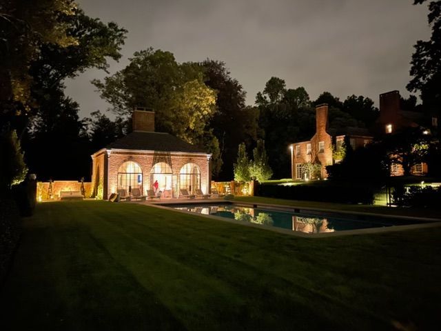 Nighttime garden estate with a lit pavilion and reflecting pool surrounded by trees