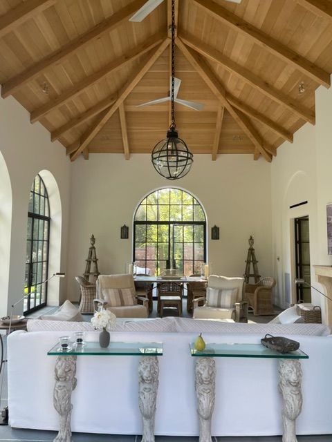 Bright living room with vaulted wood ceiling, arched windows, and white furniture with carved legs