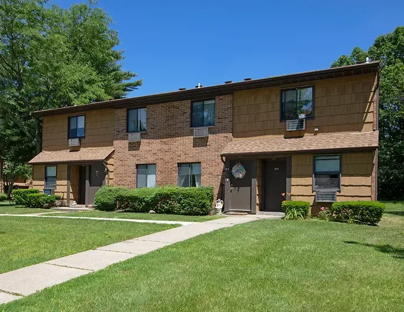 Two-story brick apartment building with green lawn and sidewalk under a clear sky