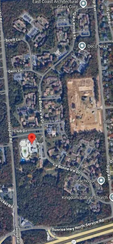 Satellite map of a neighborhood with a red location pin near a white building and a large construction site nearby