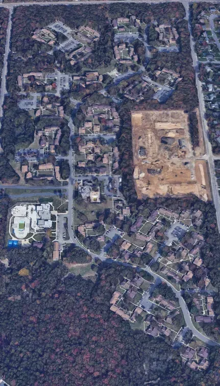 Aerial view of a wooded neighborhood with winding roads, houses, and a large tan construction site.