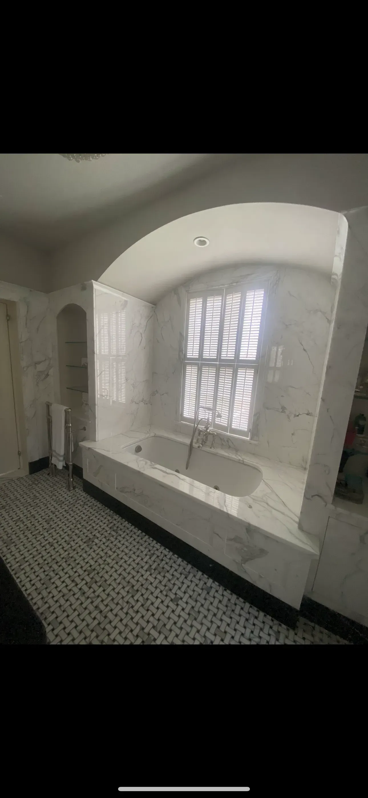 Empty tiled bathroom with a large arched window and bathtub under it.