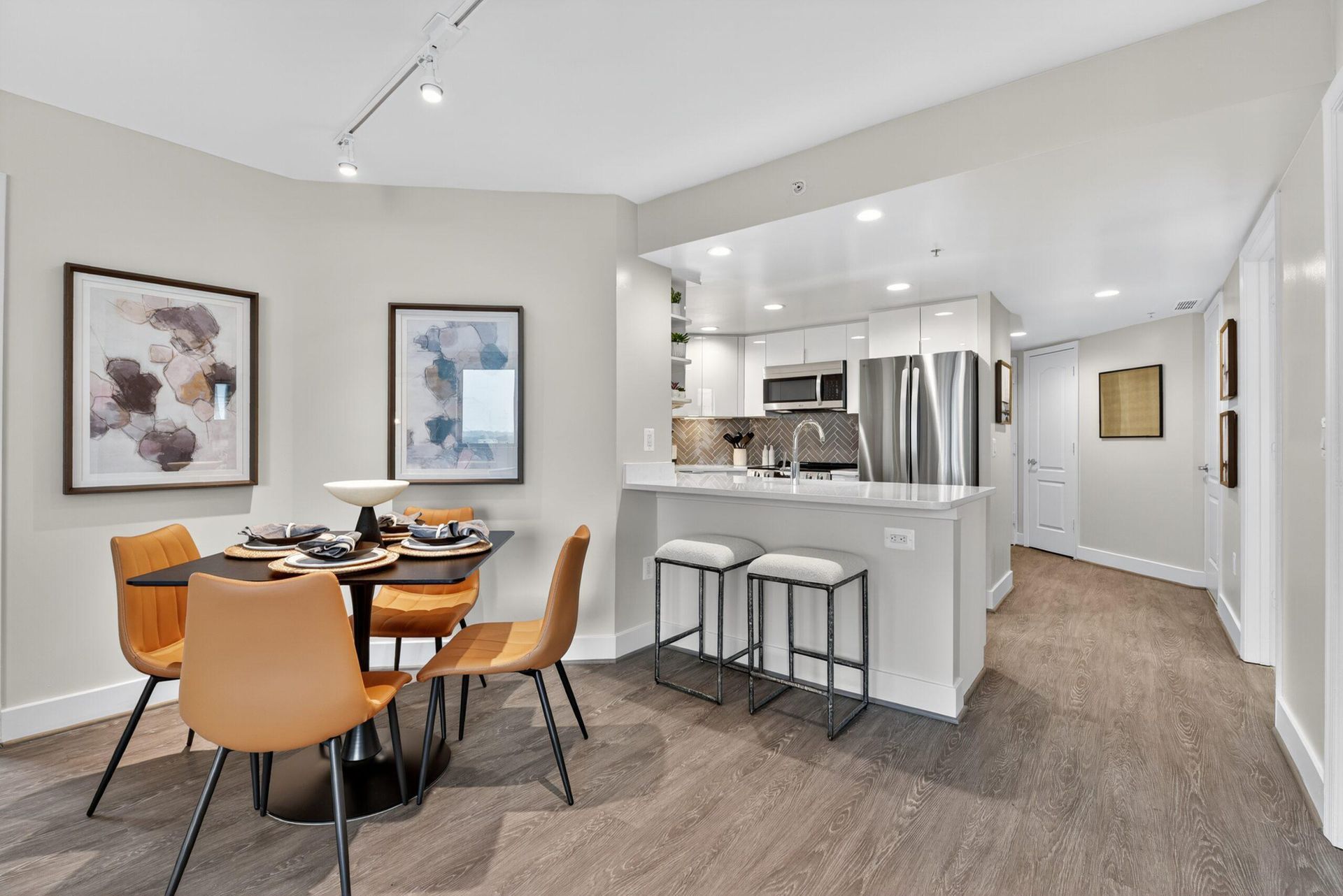 Modern kitchen and dining area with white cabinets, island stools, and a round wooden table with tan chairs.
