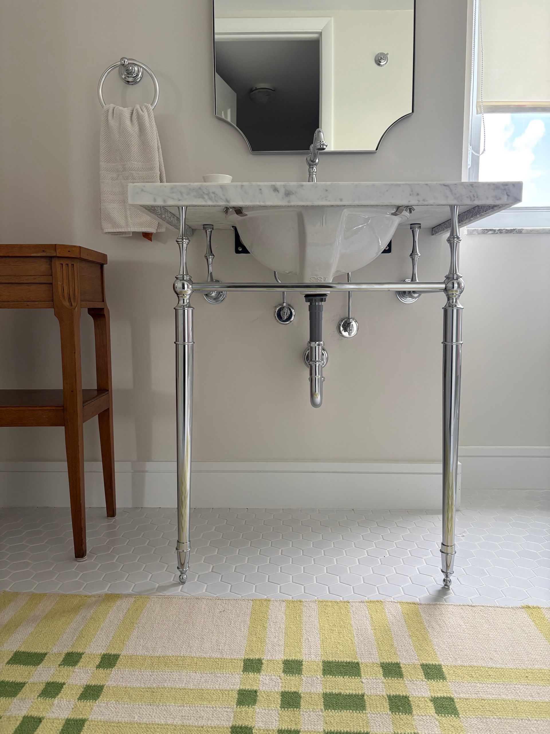 White bathroom vanity with sink and mirror above a patterned rug; a towel hangs to the left.