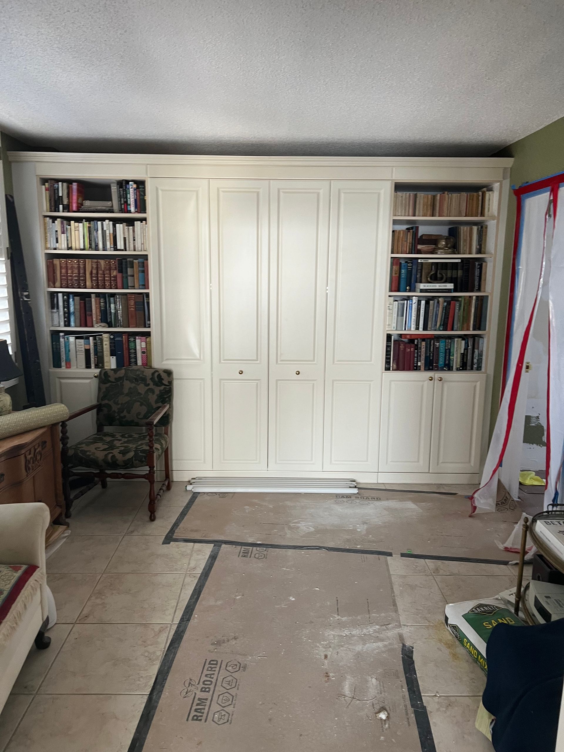A room with white built-in cabinets, bookshelves, and a partially covered floor under renovation.