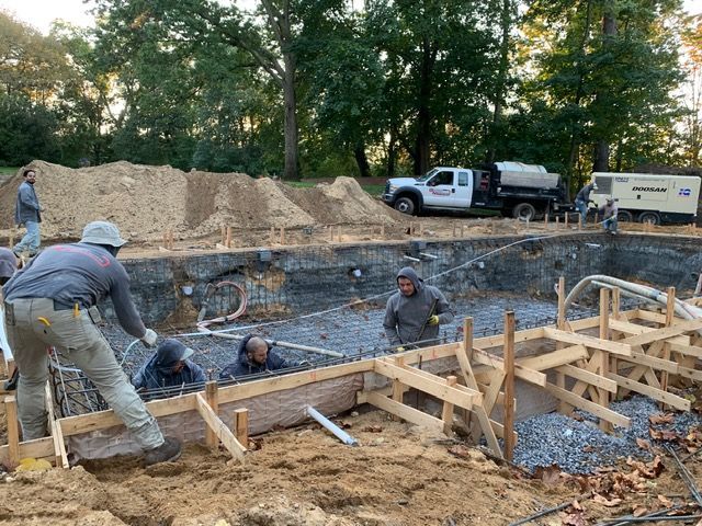 Construction workers pouring concrete for a foundation at an outdoor building site.