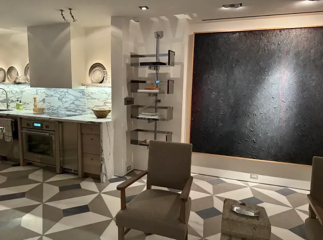 Modern lounge with patterned tile floor, two chairs, shelves, and a large black wall artwork