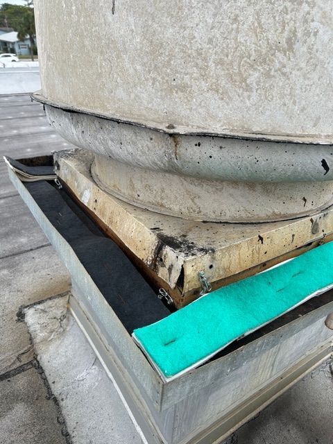Damaged rooftop base with peeling sealant and a turquoise repair strip around a concrete column
