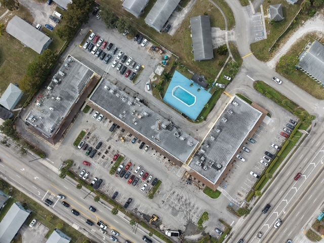 Aerial view of apartment buildings, parking lots, and a blue swimming pool beside a road
