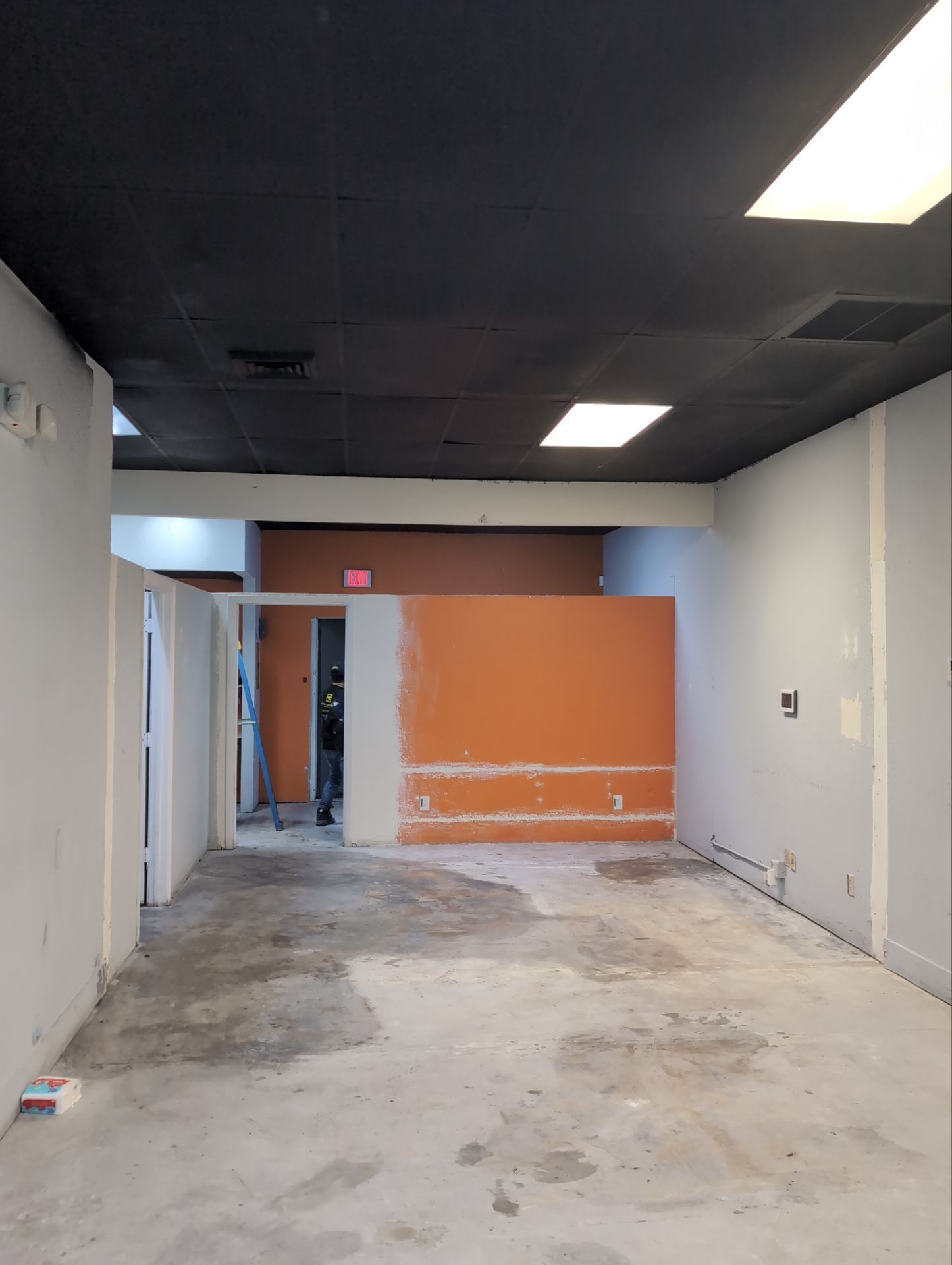 Empty commercial room with orange back wall, gray floor, and ceiling lights.