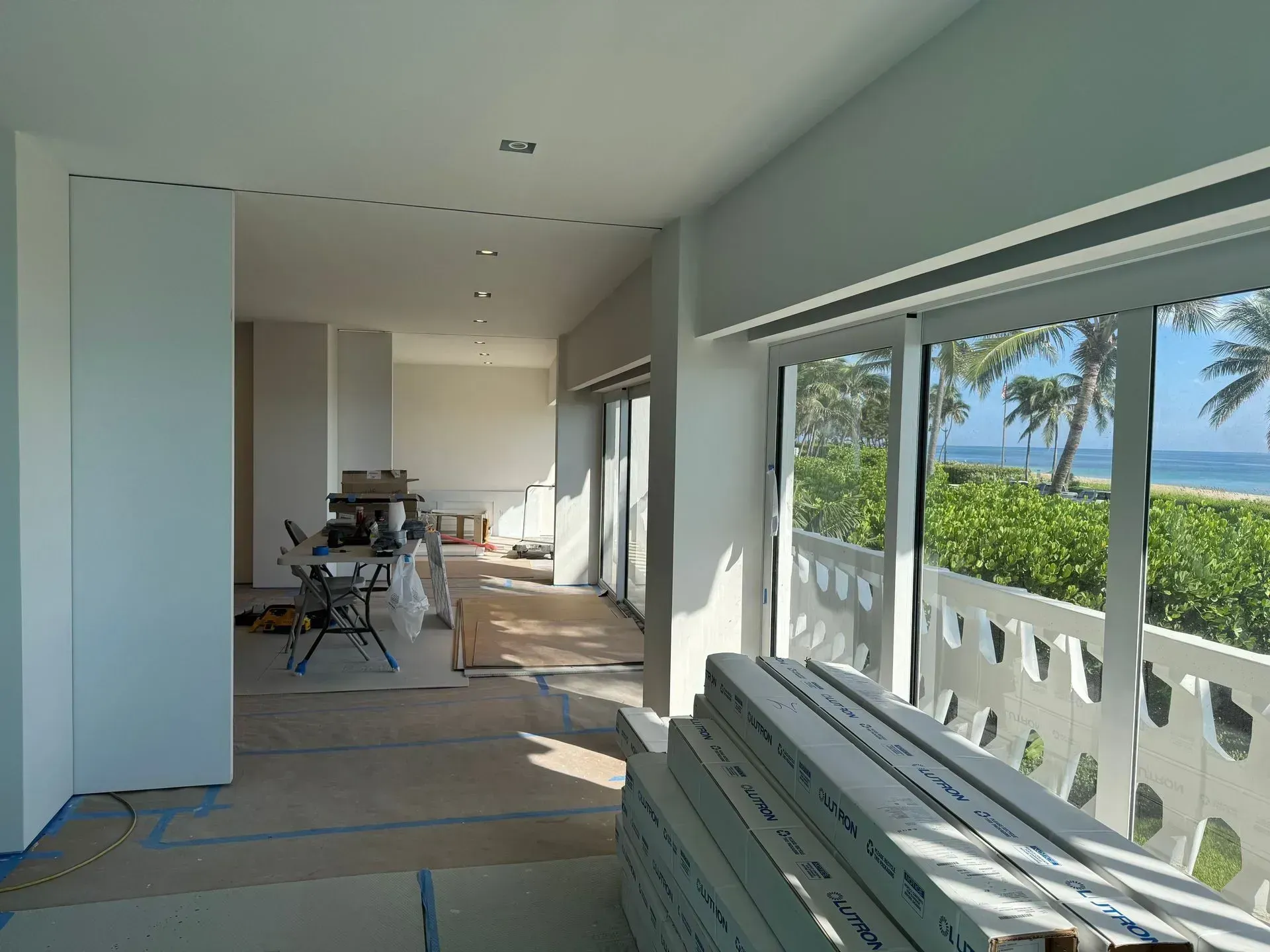 Bright hallway overlooking ocean, with large windows, white bench, and dining area in the distance.