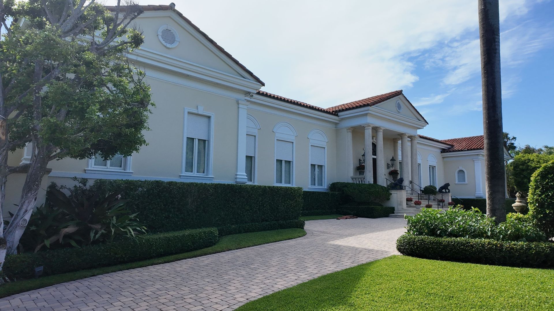 White Mediterranean-style house with a red-tiled roof, manicured hedges, and a curved walkway in front