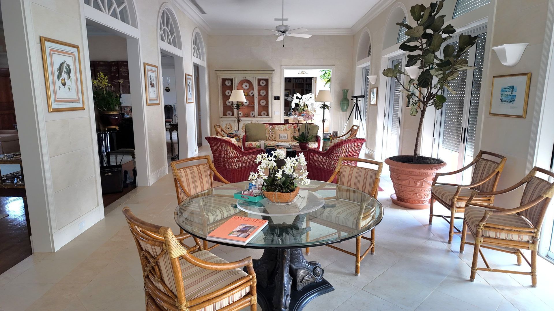 Bright living room with glass dining table, wicker chairs, potted plants, and framed wall art