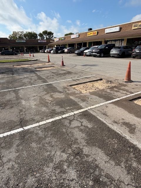 Parking lot with orange cones in front of a strip mall storefronts and parked cars