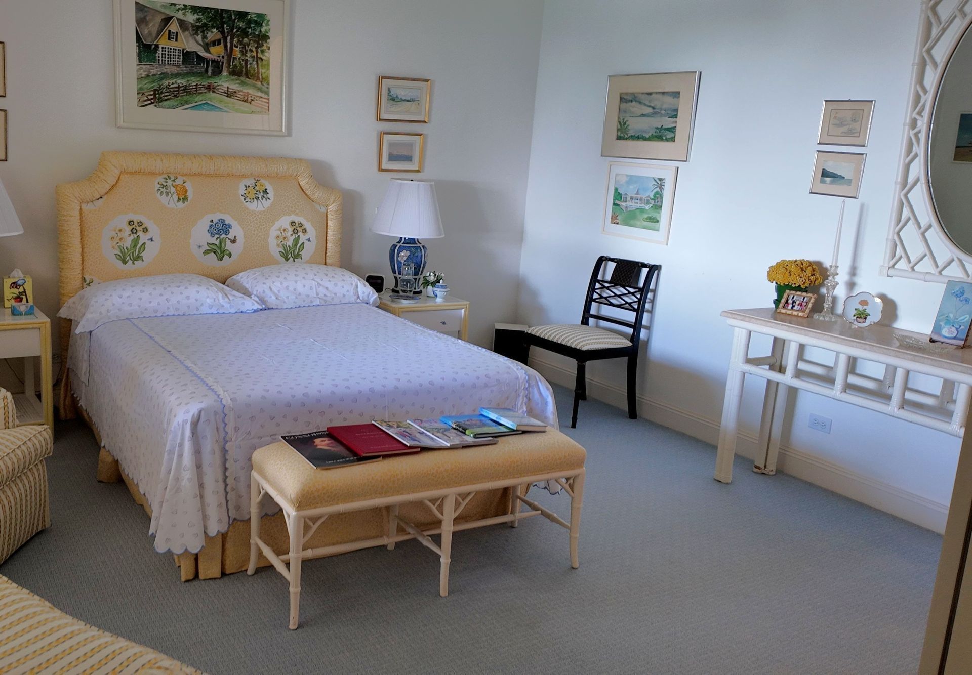 Bright bedroom with a white bed, wicker bench, desk, lamp, and framed art on the walls.