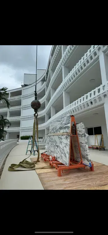 Cargo net hoisted beside a white multi-story building, with a red frame and rope on a terrace.