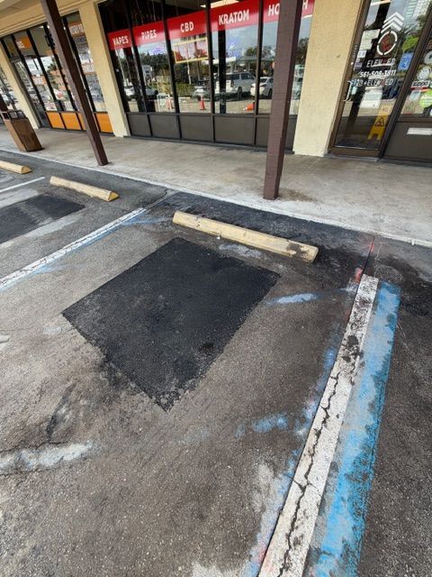 Parking lot access aisle with a curb ramp, faded painted lines, and storefronts in the background