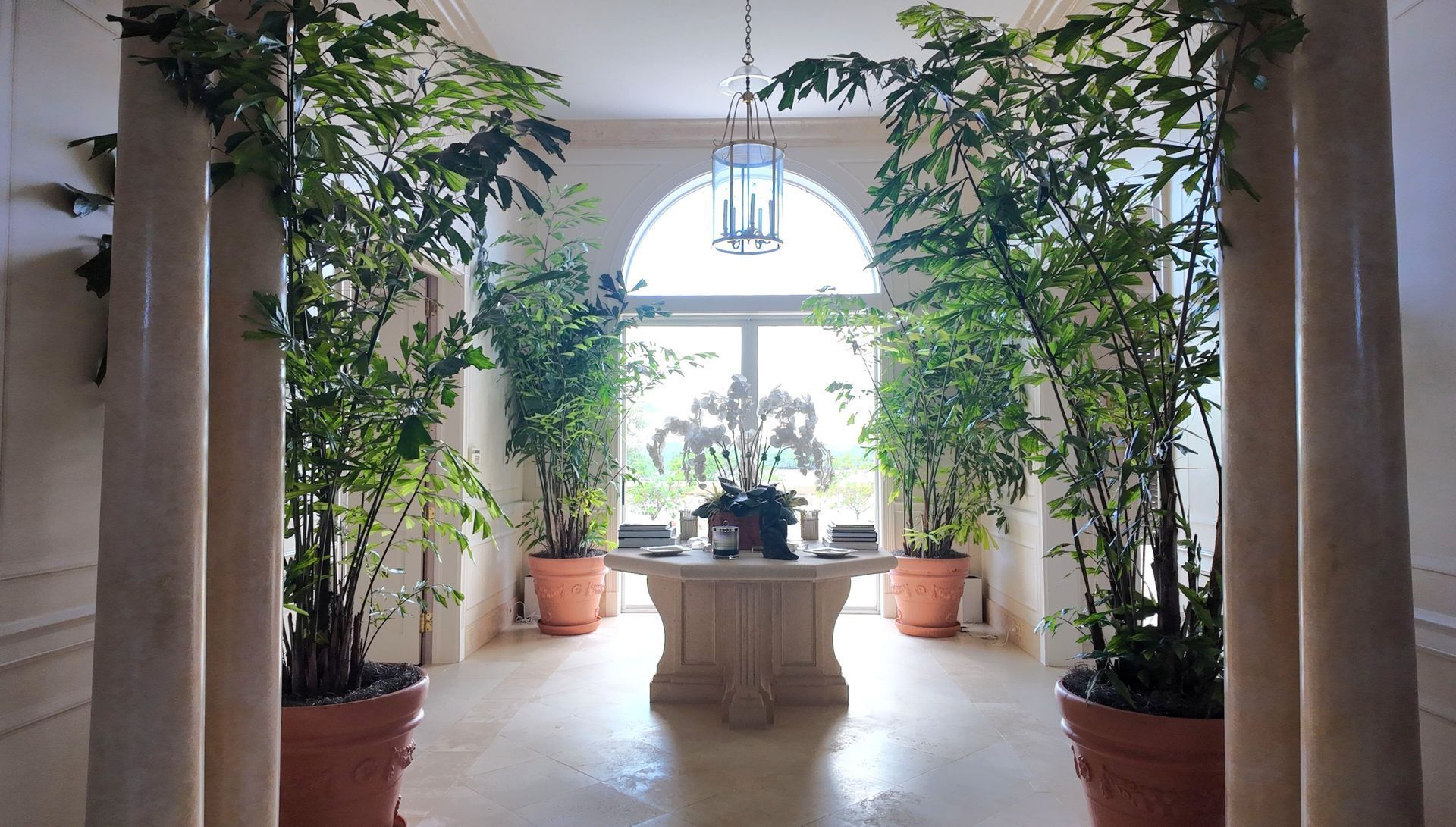 Bright indoor courtyard with potted trees, central stone table, and arched window light