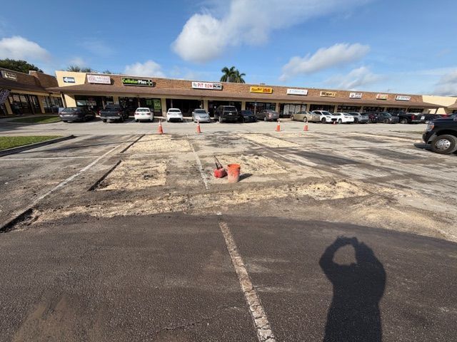 Parking lot with orange cones and a marked-off concrete area in front of a strip mall