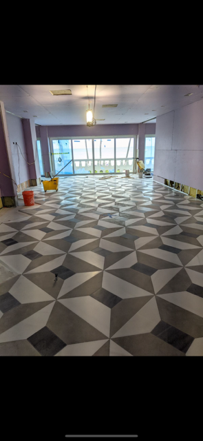 Empty modern room with geometric patterned floor, large windows, and a hanging light fixture