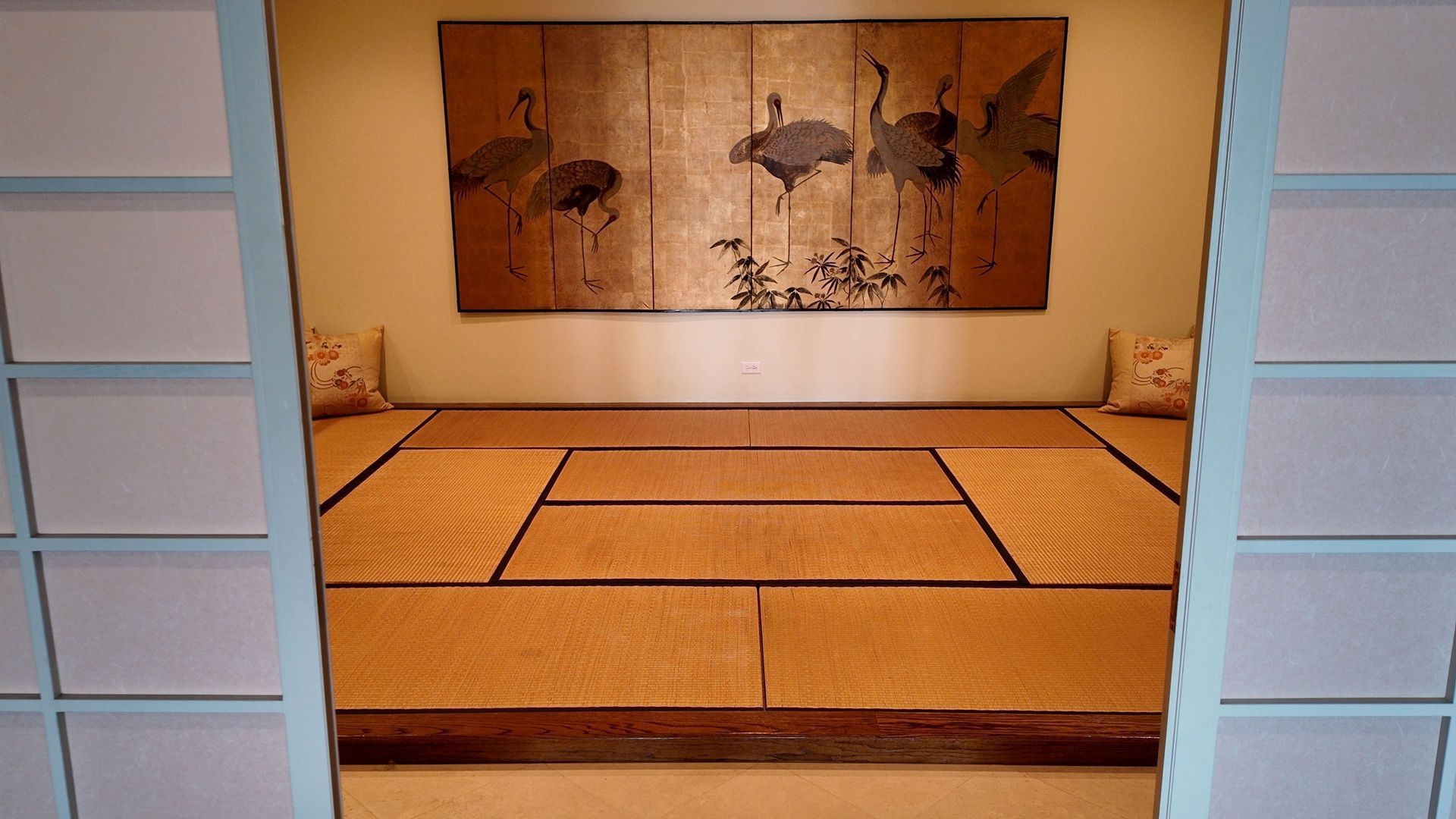 Minimalist tatami room with woven mats, low cushion seating, and a horse mural on the back wall