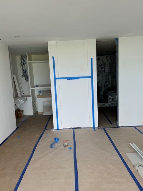 Room under renovation with taped floor, blue painter’s tape, and open closet spaces.